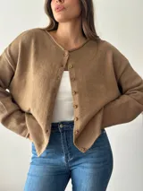 Cardigan de punto color marrón, con cuello redondo y cierre frontal de botones. Presenta mangas largas con diseño holgado y terminaciones en tejido acanalado.