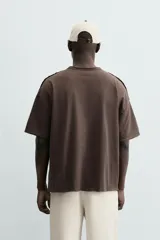 Camiseta de corte relajado (relaxed fit) color blanco roto, con cuello redondo y manga corta. Presenta un bordado sutil en el pecho con diseño floral en tonos claros.
