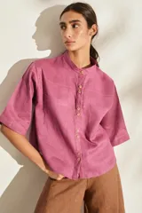Camisa de lino color fucsia, con cuello mao, mangas cortas holgadas y cierre frontal con botones de madera. Cuenta con bolsillos frontales en el pecho.