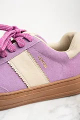 Zapatilla urbana de gamuza color lila con detalles en beige y suela marrón.