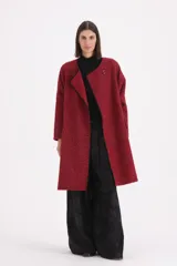 Tapado de textura bouclé en color rojo, con diseño de corte recto, sin cuello y cierre frontal mediante un único botón. Presenta un ribete en contraste de color negro que recorre los bordes de la prenda.