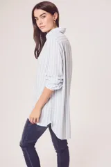 Camisa oversize celeste y blanca a rayas verticales, de mangas largas con puños abotonados y cuello camisero.