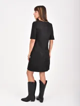 Vestido corto de corte recto y estilo minimalista, confeccionado en tela tipo gamuza negra. Presenta cuello redondo, mangas cortas y dos bolsillos frontales aplicados a la altura de la cadera.