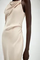 Vestido midi de escote asimétrico con una manga corta y un lado sin manga. Presenta un diseño drapeado en la parte delantera y cierre en la espalda con abertura y botones.