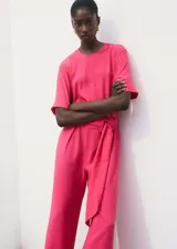 Mono largo de diseño recto en color fucsia, con cuello redondo, manga corta y cierre de botón en la parte posterior. Incluye trabillas y un cinturón de tela ajustable con hebilla en la cintura.