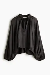 Blusa oversize corta color negro, confeccionada en tejido brillante. Presenta cuello nido de abeja con frunces y escote en V profundo, mangas globo largas de corte raglán y puños elásticos.