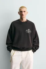 Sudadera de corte relajado color negro con efecto lavado, cuello redondo, manga larga y puños en rib. Presenta un estampado gráfico a contraste en el pecho con el texto 'General Service Goods'.
