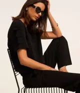 Blusa negra de crepé con cuello redondo y mangas cortas decoradas con lazos aplicados.