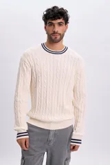 Buzo de tejido de punto con diseño de ochos, color crudo, con cuello redondo, puños y dobladillo acanalados con líneas azul marino y blancas.