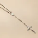 Rosario de plata 925 con cuentas esféricas pulidas, medalla central con imagen religiosa y cruz con figura de Cristo en relieve.