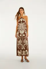 Vestido largo marrón con escote halter y espalda descubierta, confeccionado en tejido ligero con intrincados bordados en color crudo con motivos florales.