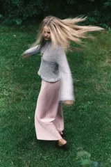 Buzo corto de punto pointelle color gris, con cuello redondo, mangas largas y terminaciones festoneadas en cuello y puños. Presenta un ribete acanalado con volados en el bajo.