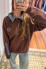 Buzo estilo rugby color bordó con cuello tipo camisa en denim azul, cierre frontal parcial y detalles de tiras laterales en las mangas. Presenta un logo bordado en el pecho con diseño de estrellas.