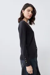 Cardigan de punto negro con escote en V, cierre frontal con botones metálicos dorados y mangas largas con puños ajustados que incluyen detalles de botones decorativos.