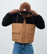 Chaqueta tipo parka de poliéster con diseño en bloques de color negro y tostado. Presenta capucha ajustable con cordones, cierre frontal con solapa superpuesta y bolsillos frontales con tapa.