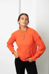 Buzo de lana color coral con diseño de tejido trenzado, cuello redondo y mangas largas.