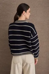 Cardigan de punto con diseño a rayas horizontales en azul marino y beige. Presenta cuello redondo, cierre frontal con botones grandes y mangas largas con puños acanalados en tono verde oliva. Incluye un pequeño bordado de una raqueta de tenis en el lateral.