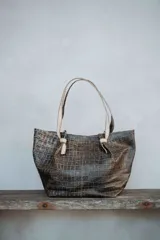 Bolso tipo tote de gran capacidad con textura efecto reptil en tonos oscuros. Presenta asas largas en color claro con detalle de nudo en la unión con el cuerpo del bolso.