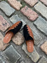 Zapatos tipo mules de punta cerrada y talón abierto, con diseño bicolor que combina cuero metalizado dorado y tono mostaza. Presentan detalles de costuras cruzadas en contraste sobre el empeine y suela baja.