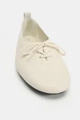 Zapato plano de piel en color blanco roto, con cierre de cordones decorativos en el empeine, punta redonda y tirador trasero.