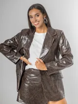 Blazer de mujer color marrón chocolate, confeccionado en ecocuero texturizado con acabado acharolado. Es forrado y presenta un corte estructurado con solapas y bolsillos frontales.
