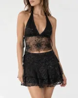 Conjunto de dos piezas de encaje negro semitransparente, compuesto por un top halter con escote en V y una minifalda con volados en cascada.
