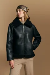 Campera tipo gamulán de cuero sintético negro, con interior y detalles de corderito sintético al tono en cuello y ruedo. Presenta cierre frontal metálico y diseño de silueta relajada.