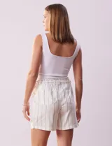 Short color crema con finas rayas verticales grises, pretina elastizada con cordón de ajuste, bolsillos delanteros y traseros.