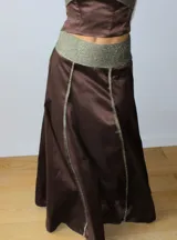 Pollera midi de corte acampanado en color verde lima con acabado satinado. Presenta una cintura alta y costuras verticales destacadas con ribetes en tejido brillante de color bordó.