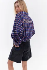 Chaqueta bomber de algodón con estampado a cuadros en tonos azules, amarillos y marrones, cuello alto y cierre frontal descentrado con botones. Cuenta con mangas abullonadas y puños elásticos.