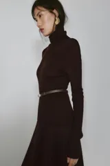 Jersey de punto liso confeccionado en 100% lana, con cuello subido y manga larga. Incluye un cinturón fino integrado en la cintura con hebilla metálica.