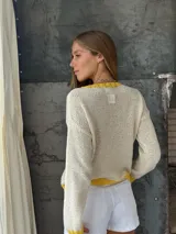 Buzo tejido de punto color blanco con diseño de corazón amarillo en el centro, cuello redondo, puños y ruedo en tono amarillo.