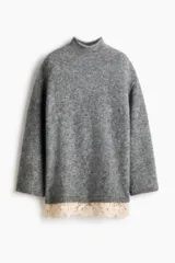 Buzo de punto holgado con mezcla de lana y mohair, color gris. Presenta cuello alto, hombros caídos y mangas largas. El bajo está decorado con un ribete de encaje en color crema en contraste.
