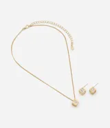 Conjunto de collar y aros color dorado, compuesto por una cadena fina con dije de cubo calado y aplicación de cristal, y caravanas haciendo juego con cierre de perno.