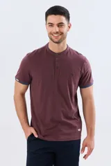Remera estilo polo con cuello mao y manga corta, de color bordó con detalles en azul en los bordes de las mangas y cuello. Cuenta con cierre frontal parcial de tres botones y pequeño logo bordado en el pecho.