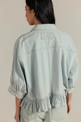Camisa de denim de corte oversize, color celeste, con bolsillos frontales, mangas abullonadas y detalle de volados en el ruedo.