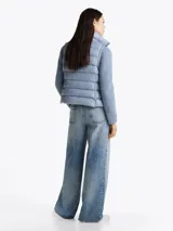 Chaleco acolchado celeste con cuello alto, cierre frontal con cremallera, dos bolsillos laterales con cremallera y logo de la marca en el pecho. Tiene mangas de tejido de punto. Repele el agua y tiene relleno de plumón.