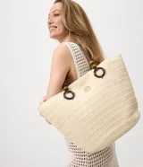 Cartera tipo bolso shopper de Bossa Nossa, confeccionada en fibra de papel color beige, con asas de hombro decoradas con cuentas de madera y aros oscuros. Cuenta con cierre de botón a presión y detalle metálico dorado frontal.