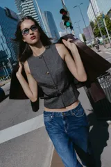 Chaleco jaspeado en tonos grises, con cuello redondo y sin mangas. Presenta cierre frontal con botones dorados y un cinturón fino negro con hebilla dorada.