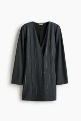 Vestido corto de punto color gris oscuro, con diseño cruzado, escote en V y aplicación de tiras de strass colgantes en el frente. Cuenta con mangas largas y hombreras.