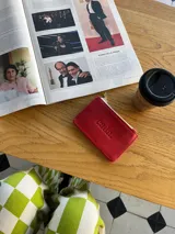 Tarjetero cuadrado de cuero rojo con cierre de cremallera dorada y la palabra "cada" grabada en el frente.