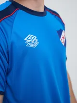 Remera deportiva de entrenamiento Umbro del Club Nacional de Football, color azul marino con detalles en blanco y líneas rojas en los hombros. Cuenta con el logo de la marca y el escudo del club en el pecho.