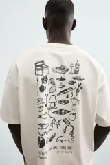 Camiseta de manga corta color blanco roto, corte relajado, con un pequeño bordado/estampado en el pecho que incluye una manzana, una rama de laurel, una trompeta y dos dados.