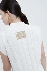 Chaleco tejido color marfil con cuello en V, sin mangas y tajos laterales.