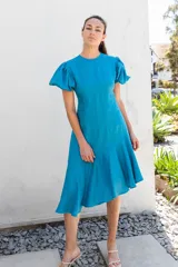 Vestido azul con escote redondo, mangas cortas abullonadas con elástico, espalda descubierta y largo asimétrico.