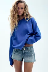 Shorts de denim de tiro bajo con cinco bolsillos, detalle de tachas, aplicación de brillos, bajo deshilachado y cierre frontal con cremallera y botones metálicos.