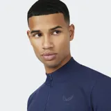 Remera deportiva de manga larga, color azul marino, con cuello alto y cierre frontal de un cuarto. Presenta un ajuste ceñido y un logo tonal en el pecho.