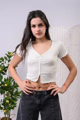 Crop top de algodón premium color blanco, de manga corta, con escote en V y cierre frontal con botones. Presenta detalles de rulos en el ruedo y las mangas.