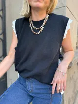 Chaleco tejido de punto en color negro, con cuello redondo a la base y diseño sin mangas. Presenta aberturas laterales con lazos ajustables que permiten regular el calce.