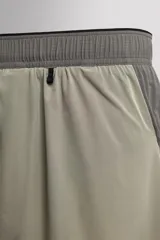 Pantalón corto de trail running color beige, confeccionado en tejidos técnicos ligeros y elásticos. Cuenta con forro interior, cintura elástica ajustable con cordón, bolsillos traseros laterales multifunción, bolsillo trasero central con cremallera, bajo con costura termofijada y aberturas laterales. Incluye logo estampado en la pernera.
